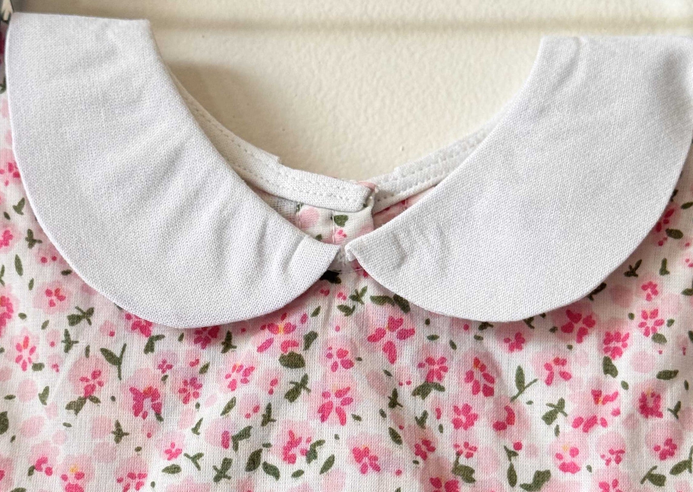 Close-up of a white Peter Pan collar on a pink floral print baby dress.