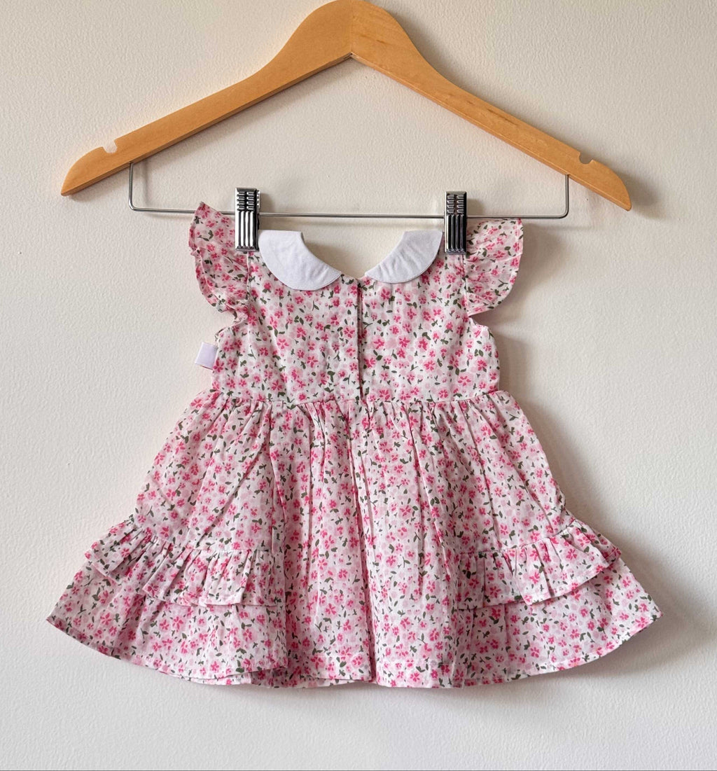 Back side of a Pink floral print baby dress with a white Peter Pan collar and ruffled sleeves
