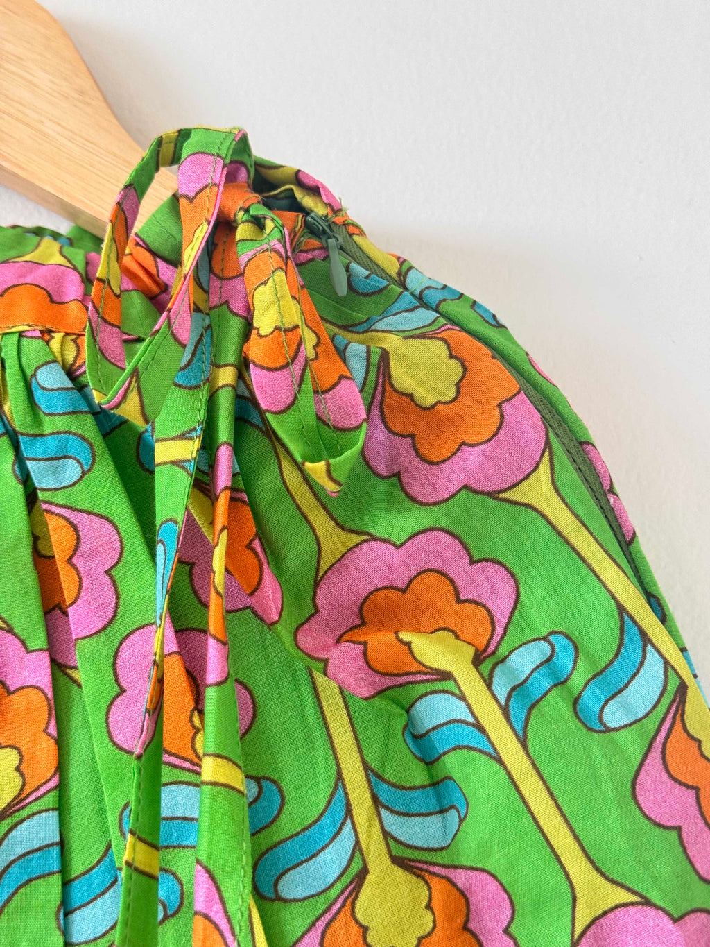 Close-up of a kids' green pure cotton choli top hanging on a wooden hanger against a plain white background. The image showcases the vibrant digital floral print in bold shades of pink, orange, yellow, and blue, emphasizing the shoulder seam and sleeveless strap design.