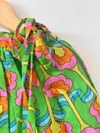 Close-up of a kids' green pure cotton choli top hanging on a wooden hanger against a plain white background. The image showcases the vibrant digital floral print in bold shades of pink, orange, yellow, and blue, emphasizing the shoulder seam and sleeveless strap design.