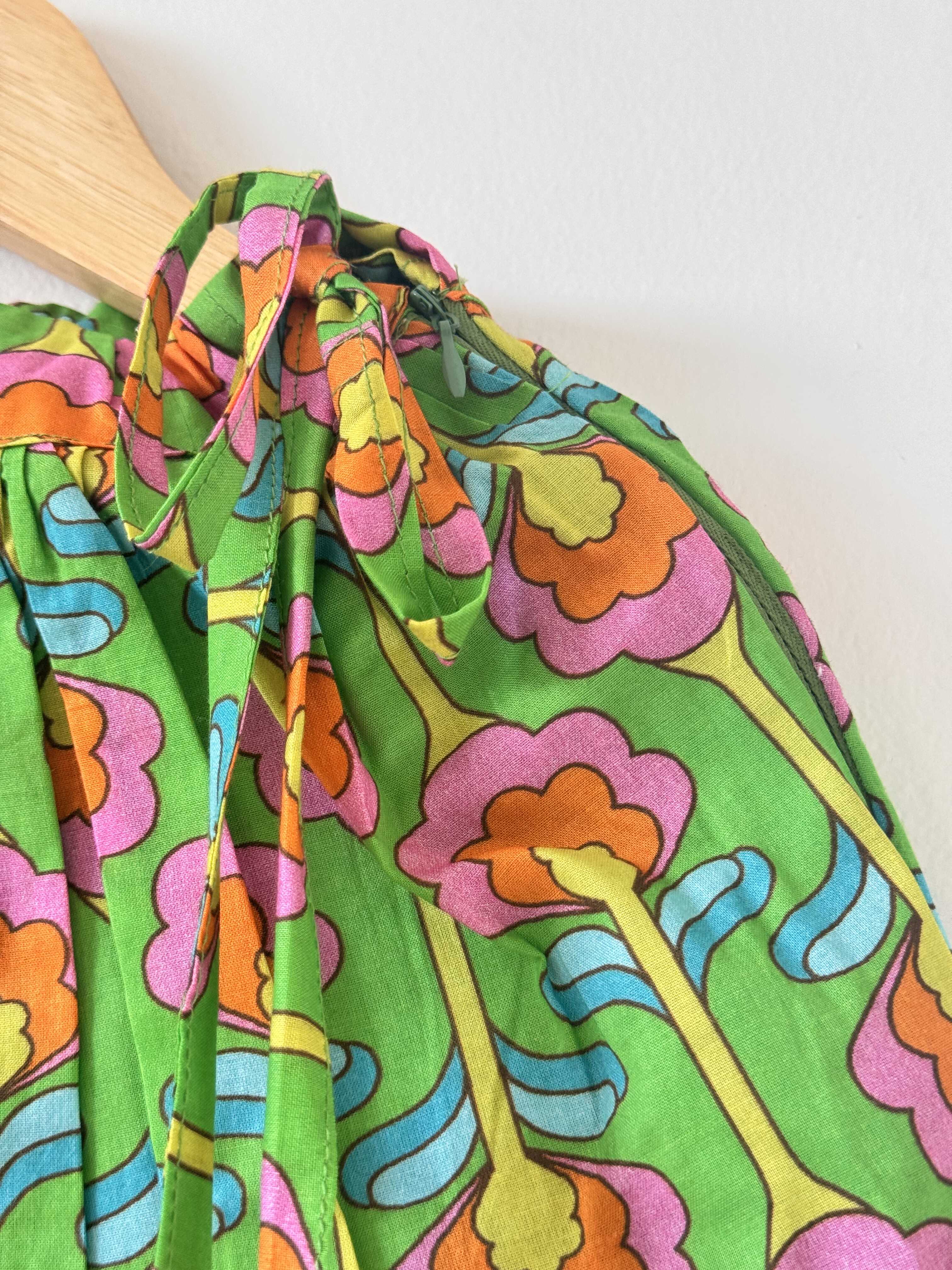Close-up of a kids' green pure cotton choli top hanging on a wooden hanger against a plain white background. The image showcases the vibrant digital floral print in bold shades of pink, orange, yellow, and blue, emphasizing the shoulder seam and sleeveless strap design.