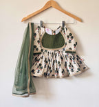 An off-white children's flared peplum kurti with green and red floral motifs, featuring a dark green pintuck yoke outlined in gold lace with a sheer green net dupatta with a gold lace border