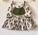 An off-white children's flared peplum kurti with green and red floral motifs, featuring a dark green pintuck yoke outlined in gold lace