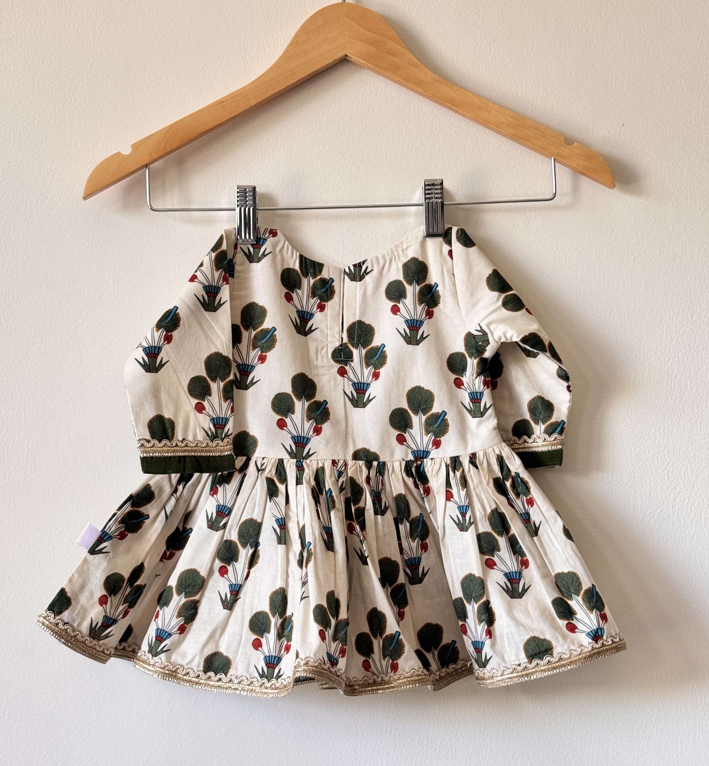 Back side of an off-white children's flared peplum kurti with green and red floral motifs